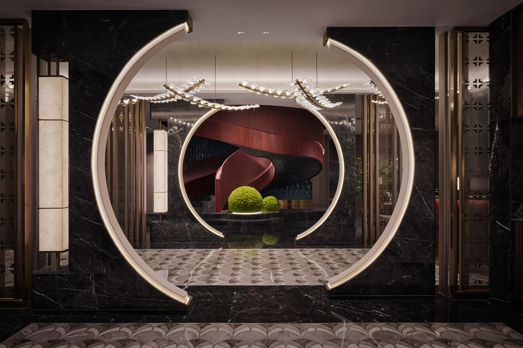 HUALUXE Zhongshan moon gate entrance framed in dark marble with a sculptural red staircase beyond.