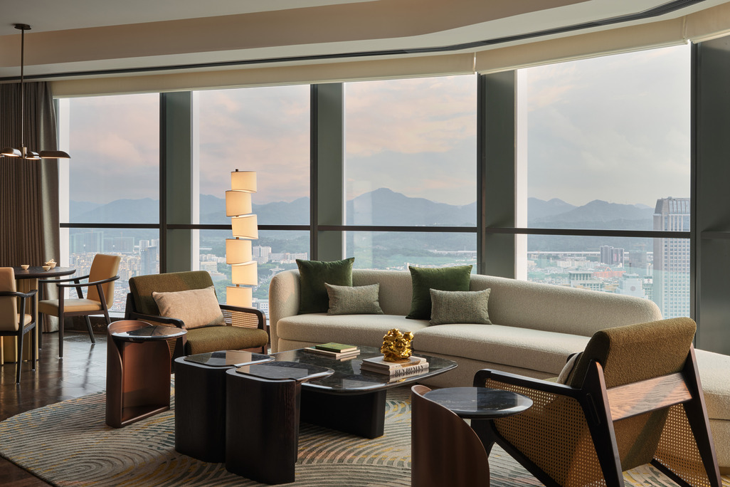 HUALUXE Zhongshan suite living area with floor-to-ceiling city and mountain views, neutral sofa and cane armchairs.
