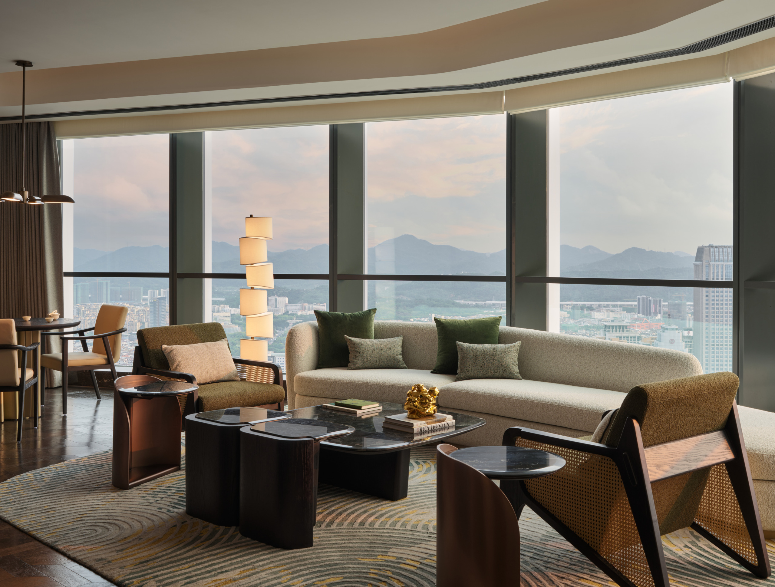 HUALUXE Zhongshan suite living area with floor-to-ceiling city and mountain views, neutral sofa and cane armchairs.