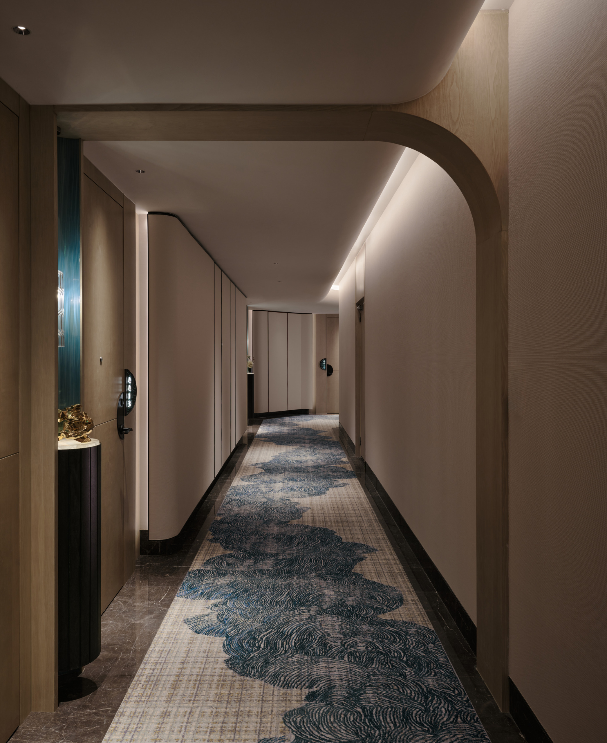 HUALUXE Zhongshan hotel corridor with patterned blue carpet runner, arched doorway and cove-lit ceiling.