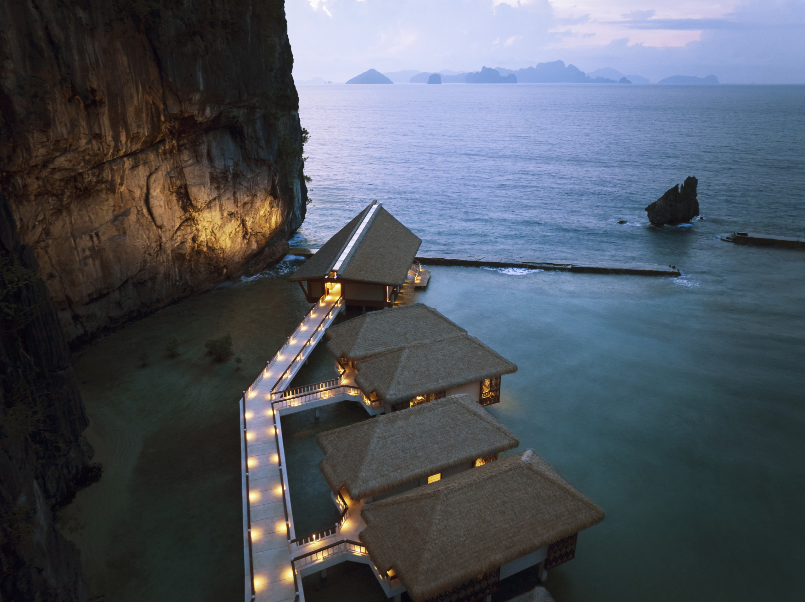 Aerial view of overwater villas at Lagen Island Resort, El Nido, nestled against limestone cliffs at dusk.
