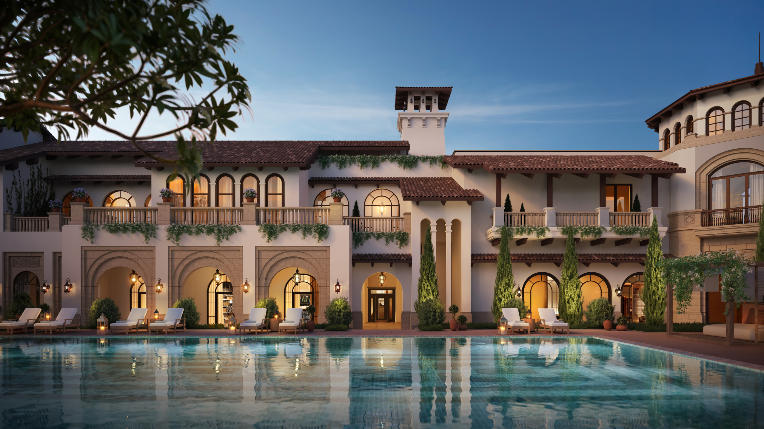 Twilight render of the Country Club at Thanh Xuan Valley, a Mediterranean-style building with arched colonnades, a tiled bell tower, and cascading terrace gardens, seen across its lit swimming pool with sun loungers along the poolside.