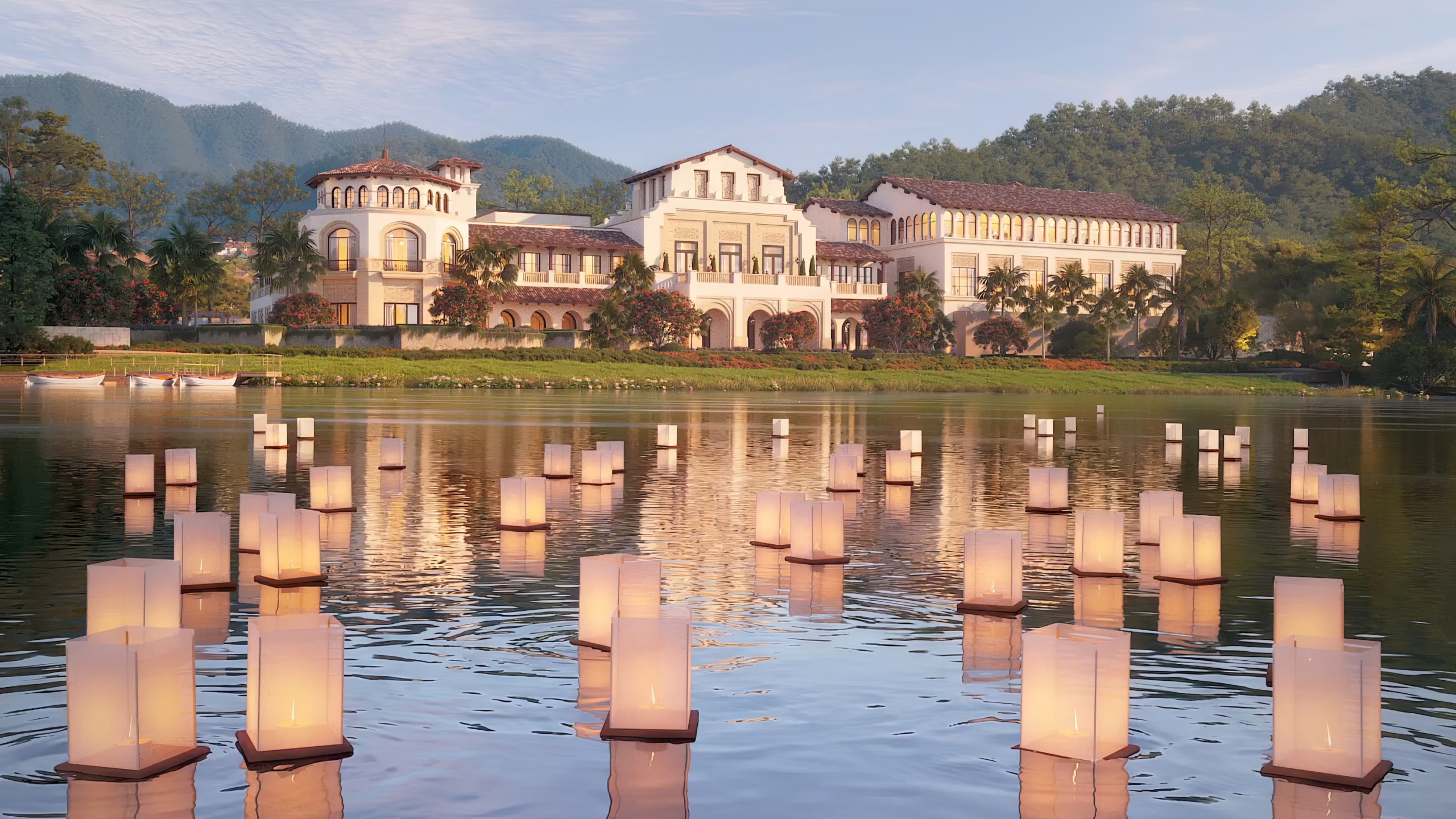 Golden-hour render of the Country Club at Thanh Xuan Valley on the lakeshore, its Mediterranean-style towers and arched colonnades reflected behind rows of floating paper lanterns on the water, with pine-forested mountains in the background.
