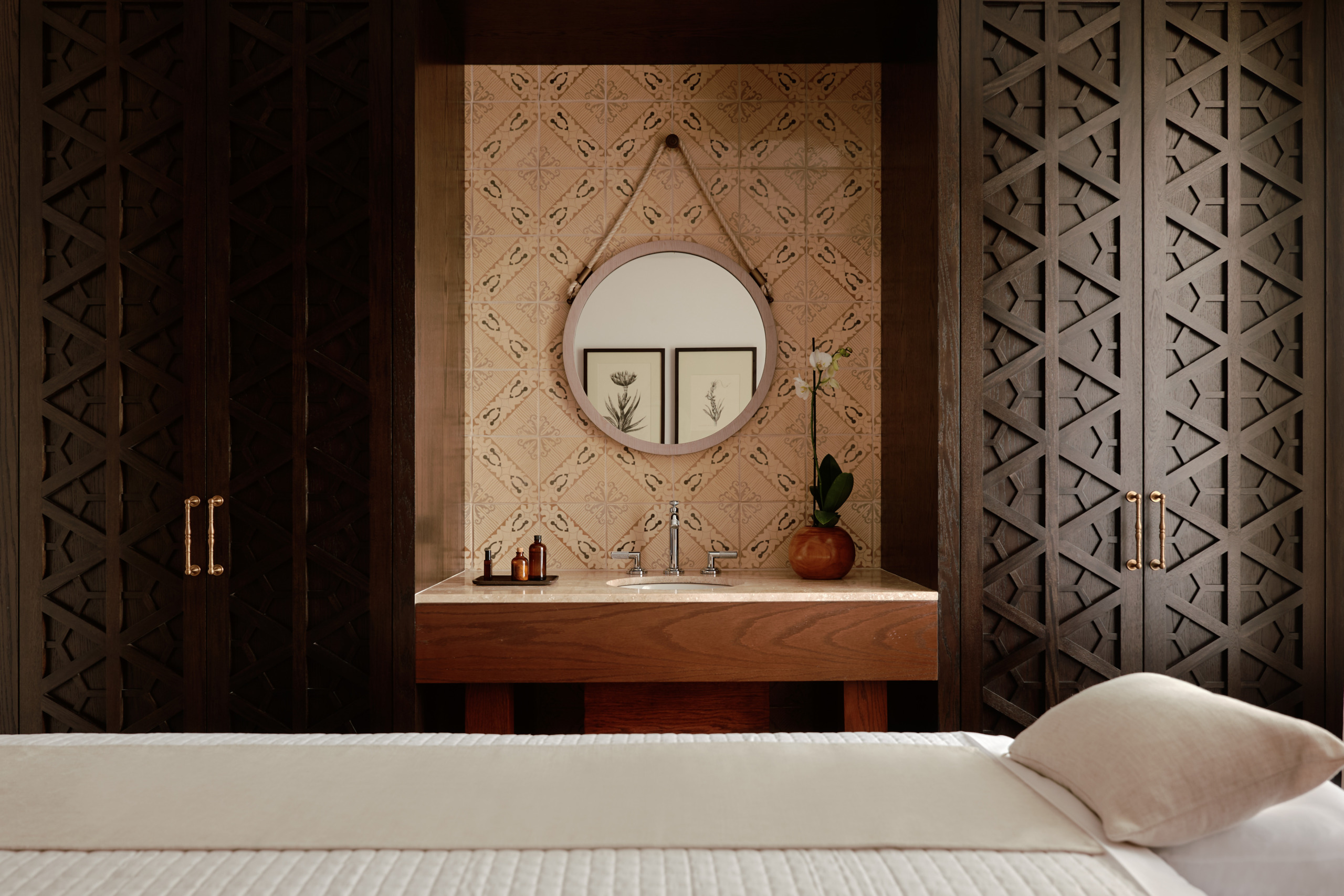 Round mirror above a stone-topped wood vanity with orchid and amber bottles, Umari Spa suite at Four Seasons Cartagena, Colombia.