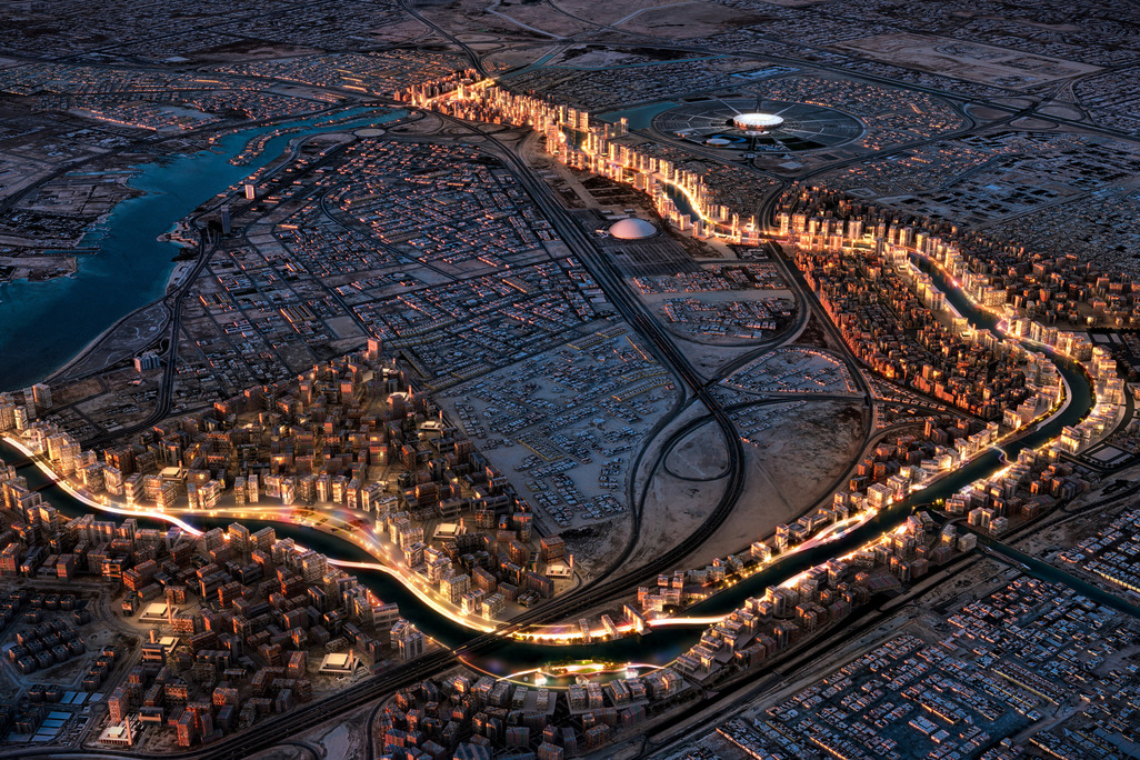 Aerial night view of Marafy waterfront development in Jeddah, Saudi Arabia, showing an illuminated canal winding through dense mixed-use buildings, with a circular stadium and open desert landscape in the background.
