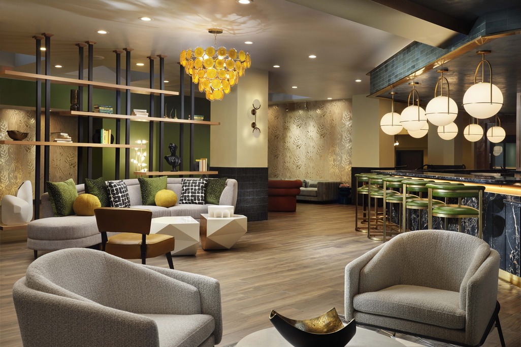 Burton House Beverly Hills hotel lobby with green velvet bar seating, amber cluster chandelier, and walnut display shelving.