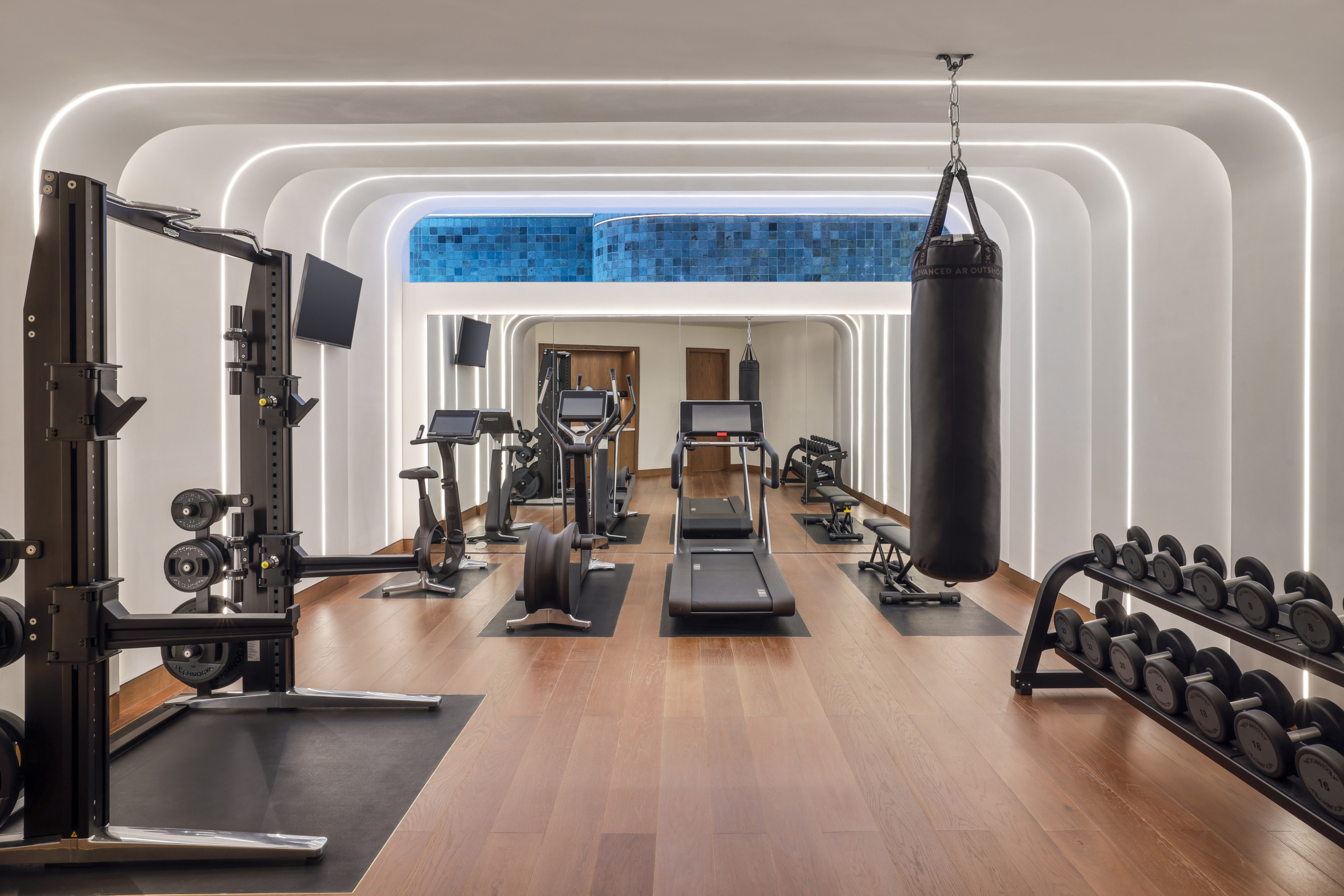 Fitness center at Waldorf Astoria Villas Lusail with treadmills, cardio machines, free weights, and a punching bag beneath arched LED-lit ceiling coves.