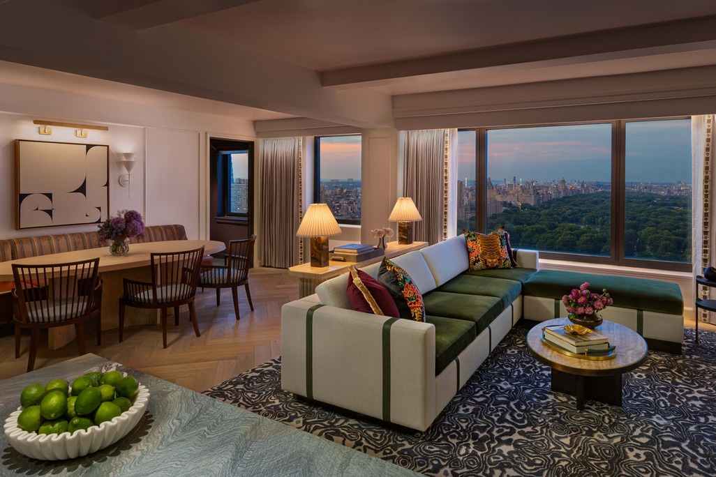 Promenade Suite living and dining area at dusk with green sectional sofa, dining table, and floor-to-ceiling views of Central Park, JW Marriott Essex House.