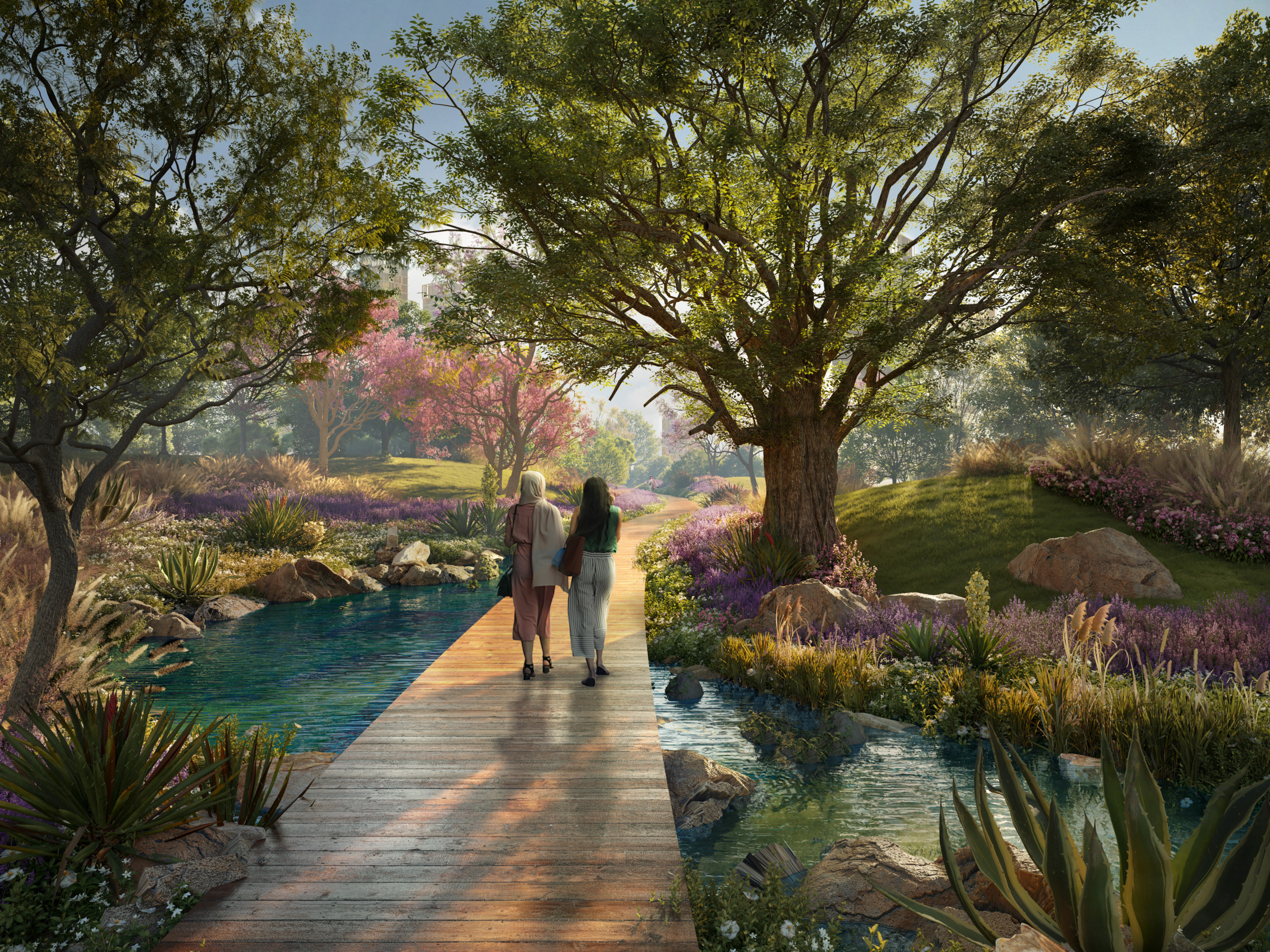 Daytime rendering of two women walking along a wooden boardwalk through a lush garden landscape, surrounded by flowering shrubs, mature trees, and a winding water channel, with a distant building visible through the foliage.