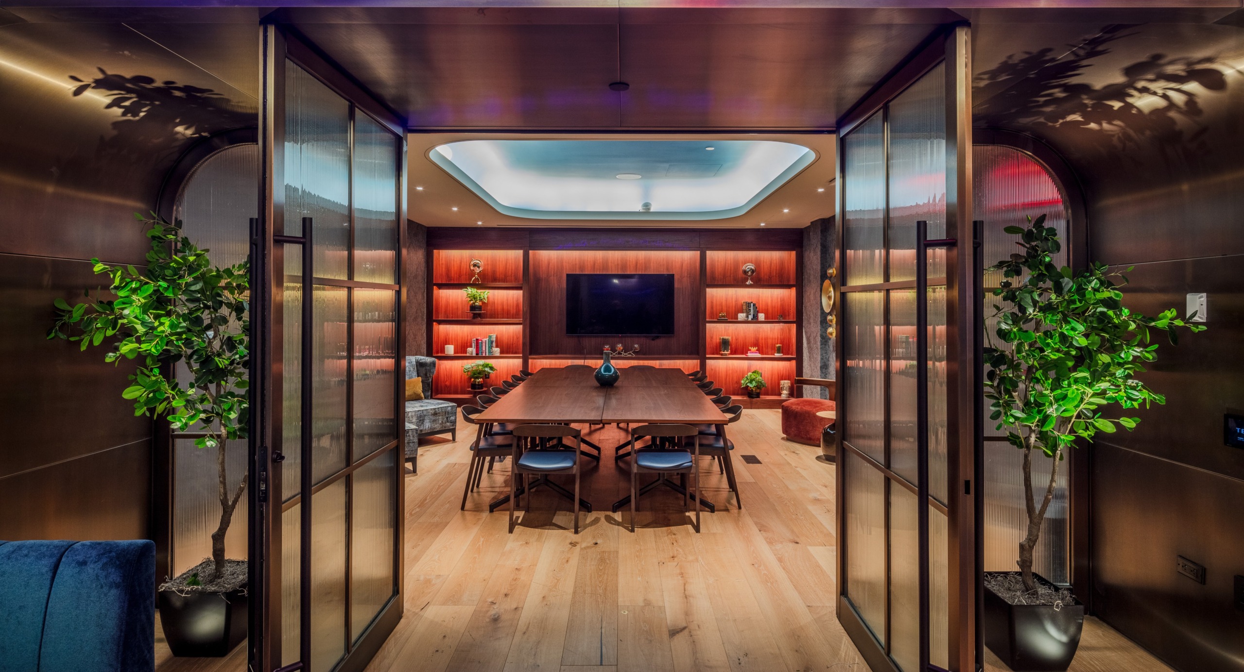 View through open doors into a private dining room at Tempo by Hilton Times Square, with a long walnut table, built-in illuminated shelving, and a wall-mounted TV.