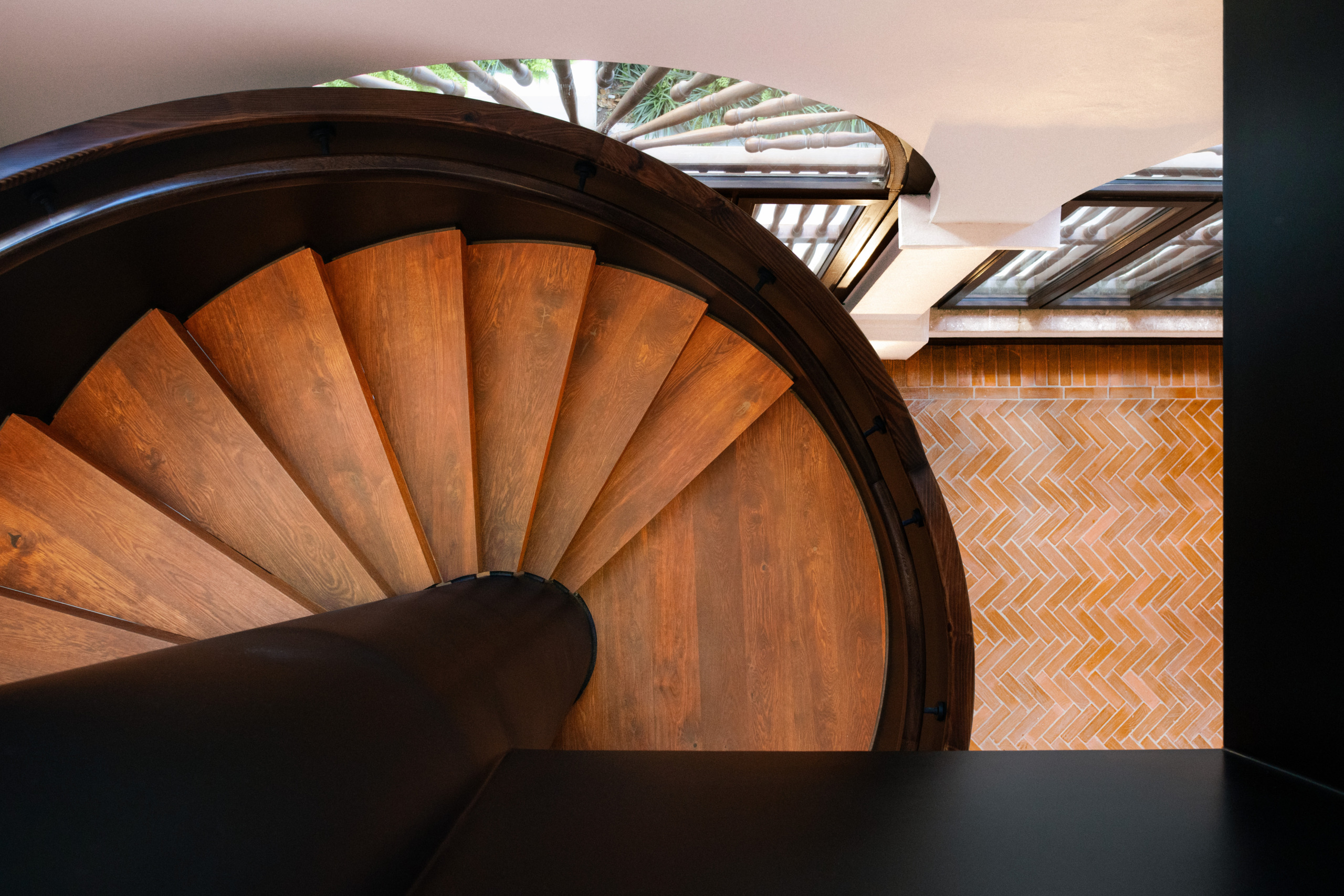 Overhead view of Umari Spa's wood spiral staircase at Four Seasons Cartagena, showing fanned wooden treads against a herringbone brick floor below.
