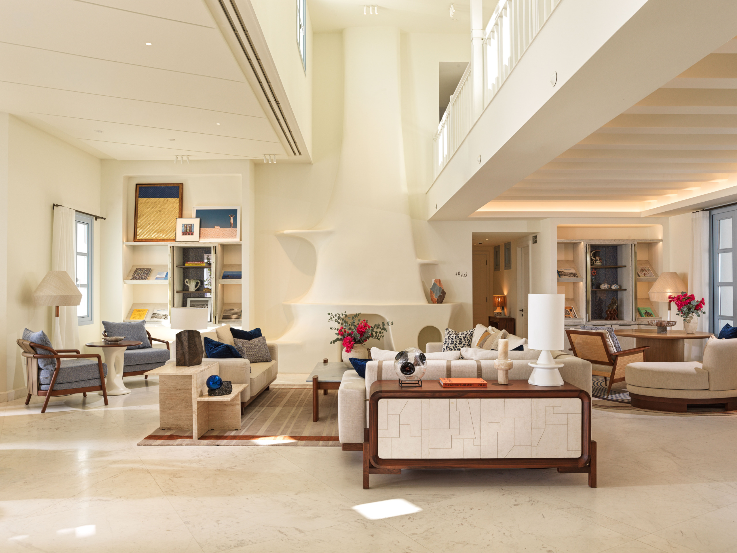 Lobby living room at Four Seasons Mykonos with a sculptural whitewashed fireplace, cream sofas, a walnut console and marble floors.