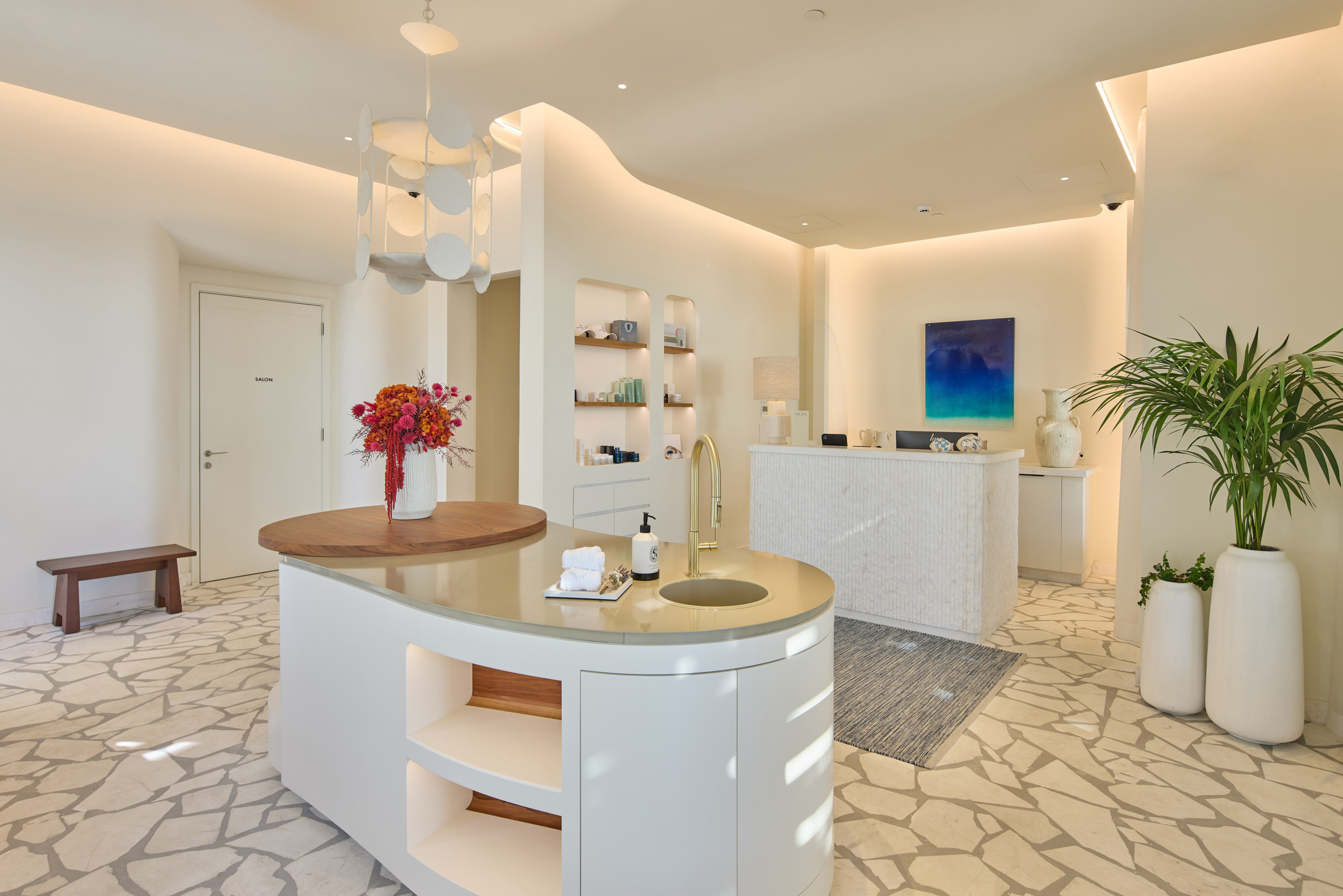 Spa reception at Four Seasons Mykonos with an asymmetric marble floor, curved white island with brass tap and marble desk.